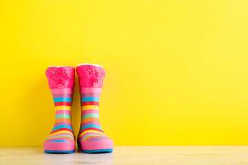 Colorful kid rubber boots on wooden floor at bright yellow wall background. Closeup. Front view....