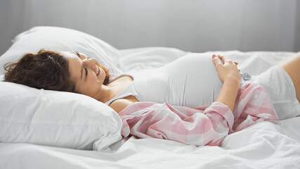 happy young woman touching belly while lying in bed