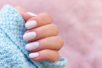 Female hand in blue knitted sweater with beautiful manicure - white ivory nails on blurred pale...