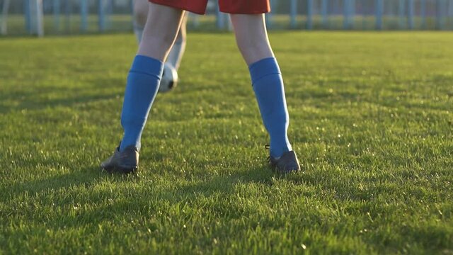 Close up of legs of two young people playing football during practice of soccer junior team. They are playing on green grass.