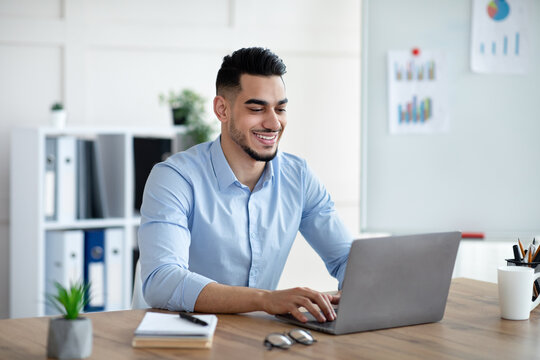 Handsome young Arab businessman working with laptop computer at his desk in office