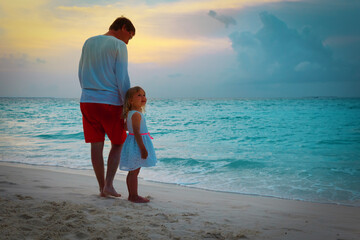 father and happy little daughter walking on beach at sunset