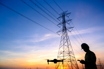 Silhouette of an electrical engineer flying a drone inspecting electricity at the station to see...