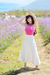 Asian beautiful woman, long hair in cute dress on Verbena filed in winter with blue sky. Beautiful cute girl portrait enjoying flowers in flowers farm background. Travel in nature outdoor concept.