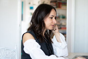 Concentrated young beautiful businesswoman working on laptop in bright home office, Books and living room in the background