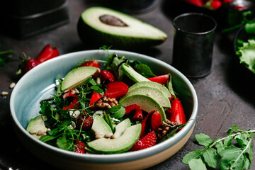 Salad with strawberries, avocado and arugula in a plate on the table. Vegetarian salad