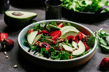 Salad with strawberries, avocado and arugula in a plate on the table. Vegetarian salad