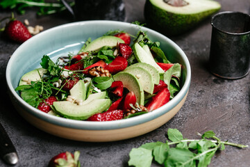 Salad with strawberries, avocado and arugula in a plate on the table. Vegetarian salad