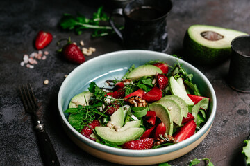 Salad with strawberries, avocado and arugula in a plate on the table. Vegetarian salad