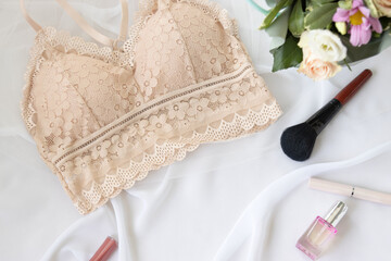 Woman elegant nude lace bra flowers, jewelry, perfume on a white background. Stylish lingerie flat lay. Underwear fashion concept