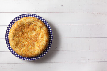 Tortilla de Patatas española. Delicioso plato salado basado en Huevo, Patatas y a veces Cebolla. En fondo de madera blanca, entera y sin cortar. 
