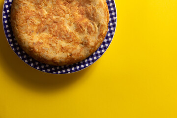 Tortilla de Patatas española. Delicioso plato salado basado en Huevo, Patatas y a veces Cebolla. En fondo amarillo, entera y sin cortar. 
