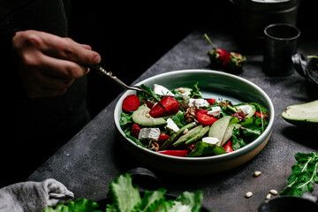 Salad with strawberries, feta, avocado and arugula in a plate on the table. Vegetarian salad