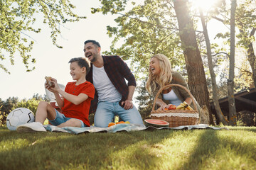 Happy young mother and father with little boy smiling while having picnic outdoors