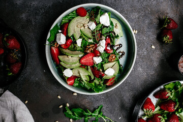 Salad with strawberries, feta, avocado and arugula in a plate on the table. Vegetarian salad