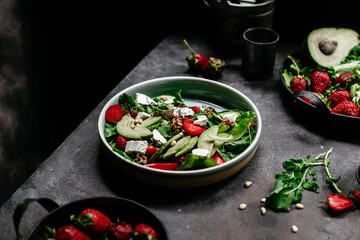 Salad with strawberries, feta, avocado and arugula in a plate on the table. Vegetarian salad