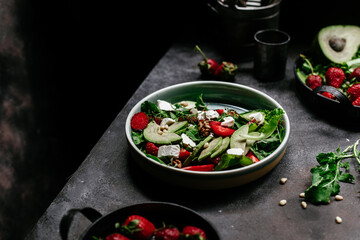 Salad with strawberries, feta, avocado and arugula in a plate on the table. Vegetarian salad