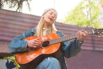 A beautiful teenage girl is playing acoustic guitar outdoors.