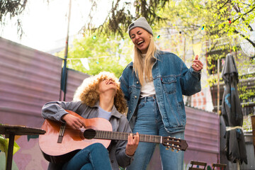 Two teenage girls are playing guitar, singing, and having fun outdoors.