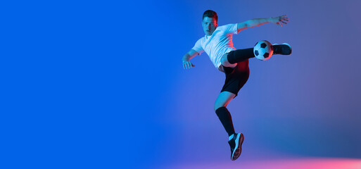 Young Caucasian man, male soccer football player training isolated on gradient blue pink background...
