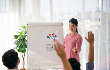Fototapeta na wymiar Smiling millennial female coach or presenter talk interact with multiracial colleagues at meeting, happy young woman tutor make flip chart whiteboard presentation at office briefing