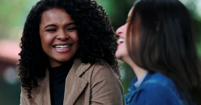Two girlfriends laughing and smiling together in conversation outside at park