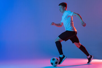 Young Caucasian man, male soccer football player training isolated on gradient blue pink background in neon light