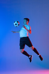 One male soccer football player in action and motion isolated on gradient blue pink background in...