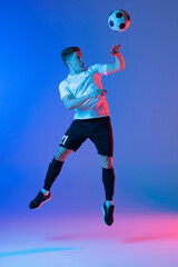 Young Caucasian man, male soccer football player jumping isolated on gradient blue pink background...