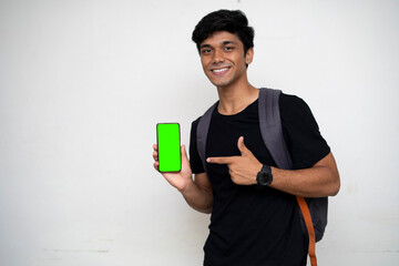 Young Indian college student holding a phone with green screen and point towards it with a smile on...