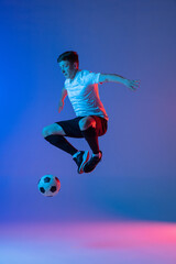 Naklejka na ściany i meble Young Caucasian man, male soccer football player training isolated on gradient blue pink background in neon light