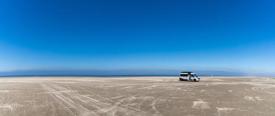 panorama of a gray camper van parked on an endless white sand beach in the middle of nowhere with...