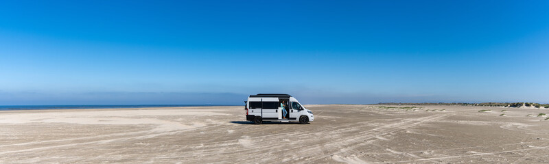 Fototapeta na wymiar panorama of a gray camper van parked on an endless white sand beach in the middle of nowhere with ocean behind