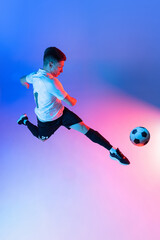 Fototapeta na wymiar High angle view of young man, male soccer football player training isolated on gradient blue pink background in neon light.