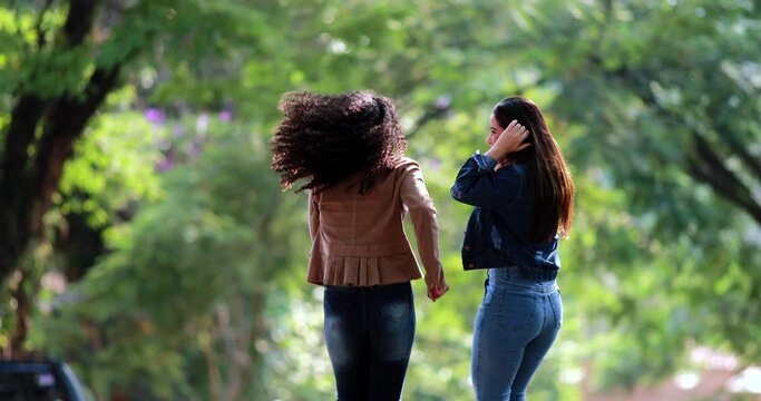 Two young women dancing in celebration outside, back view of two girls dance