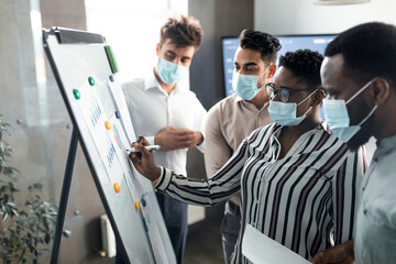 Black manager in medical mask presenting business strategy on whiteboard