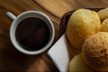 Uma xícara branca cheia de café e uma pequena cesta de vime com pães de queijo sobre uma...
