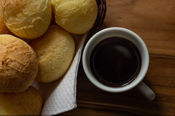 Uma xícara branca cheia de café e uma pequena cesta de vime com pães de queijo sobre uma superfície de madeira.