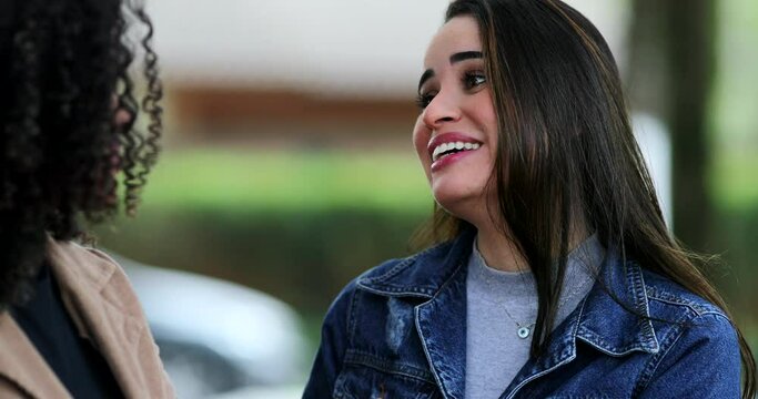 Two young women in conversation outside laughing and smiling, woman candid suprise to gossip