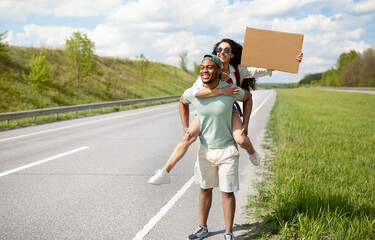 Millennial multiracial couple traveling by autostop, hitchhiking, looking for transport, holding...