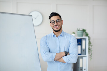 Online learning during covid. Friendly Arab teacher posing near empty blackboard with crossed arms at home office