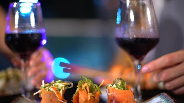 manos de una pareja tomando una copa de vino tinto y degustando un plato de sushi en un restaurante japonés