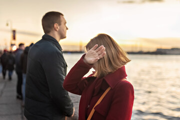 Young couple man and woman in a quarrel, on the embankment of the river in the city at sunset. The girl covered her face with her hand, crying. Emotions