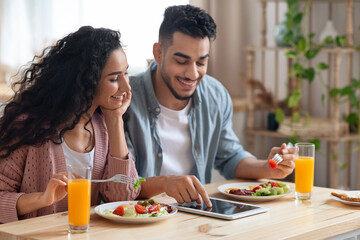 Middle-Eastern Couple Shopping Online With Digital Tablet While Having Breakfast In Kitchen