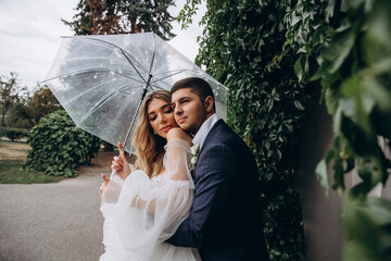Walking the bride and groom under an umbrella in a summer park. Rainy day. Newlyweds in seclusion.