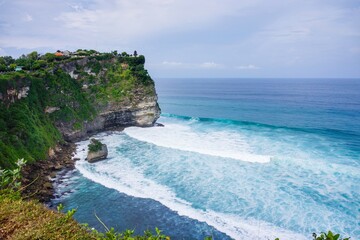 View of Uluwatu temple on a cliff by the blue sea and wave on beach. No people.