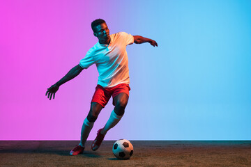 One African man, professional soccer football player training isolated on gradient blue pink...