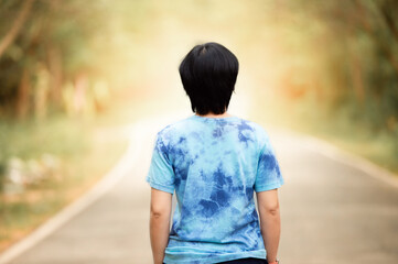Fototapeta premium woman stand on the road with tree around, Asian traveler girl stand turn back on the road with sunshine and tree of parkland