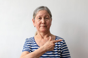 An elderly woman, a gray-haired lady of the 60s in a striped white and blue dress, pointing with her hand and finger to the side.