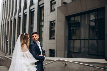 Fototapeta premium A romantic walk of the bride and groom through the city streets. Bride with a bouquet of white roses. Newlyweds on the background of the boutique.